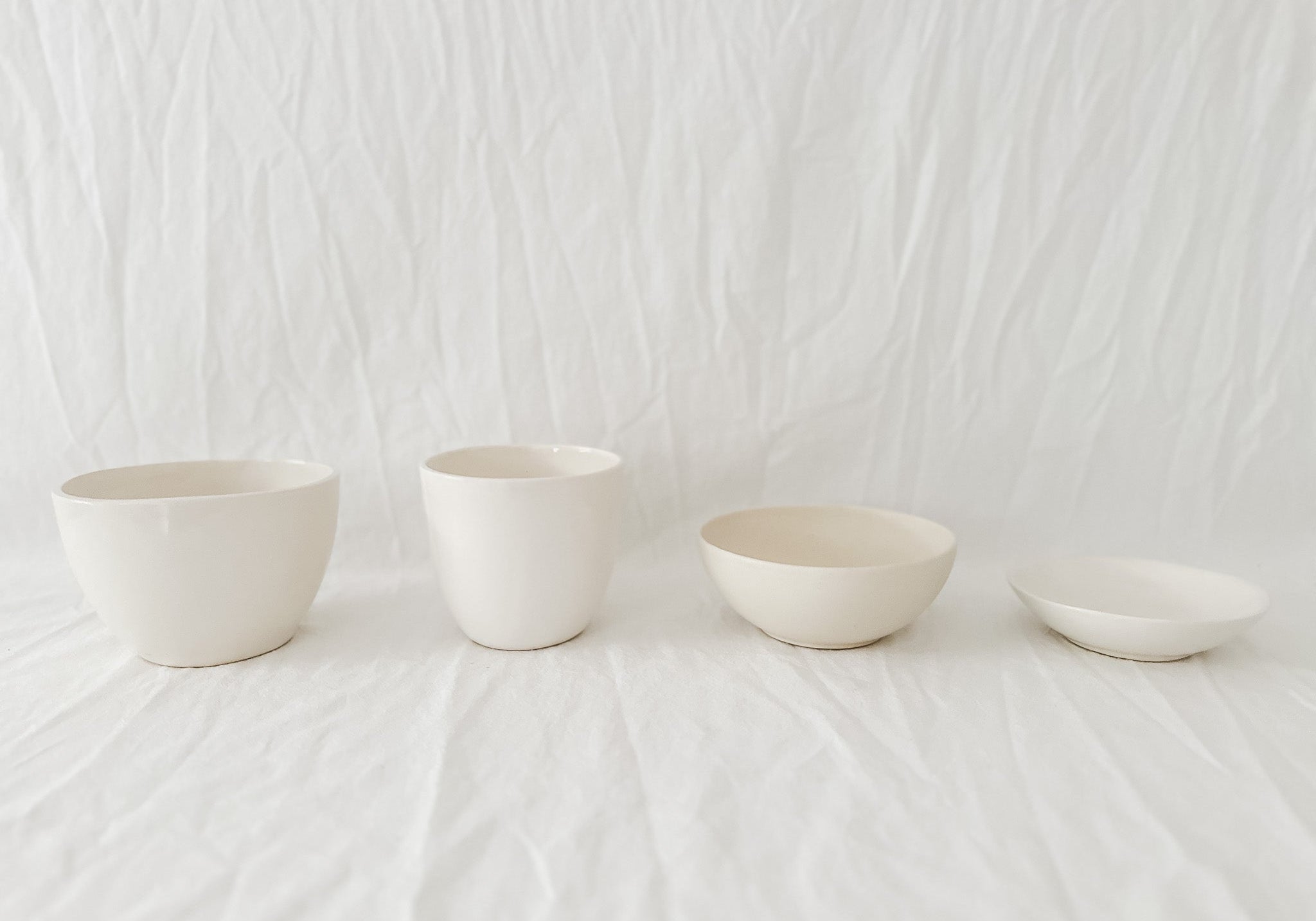 Small group of pale handmade ceramic studio samples arranged against white linen.
