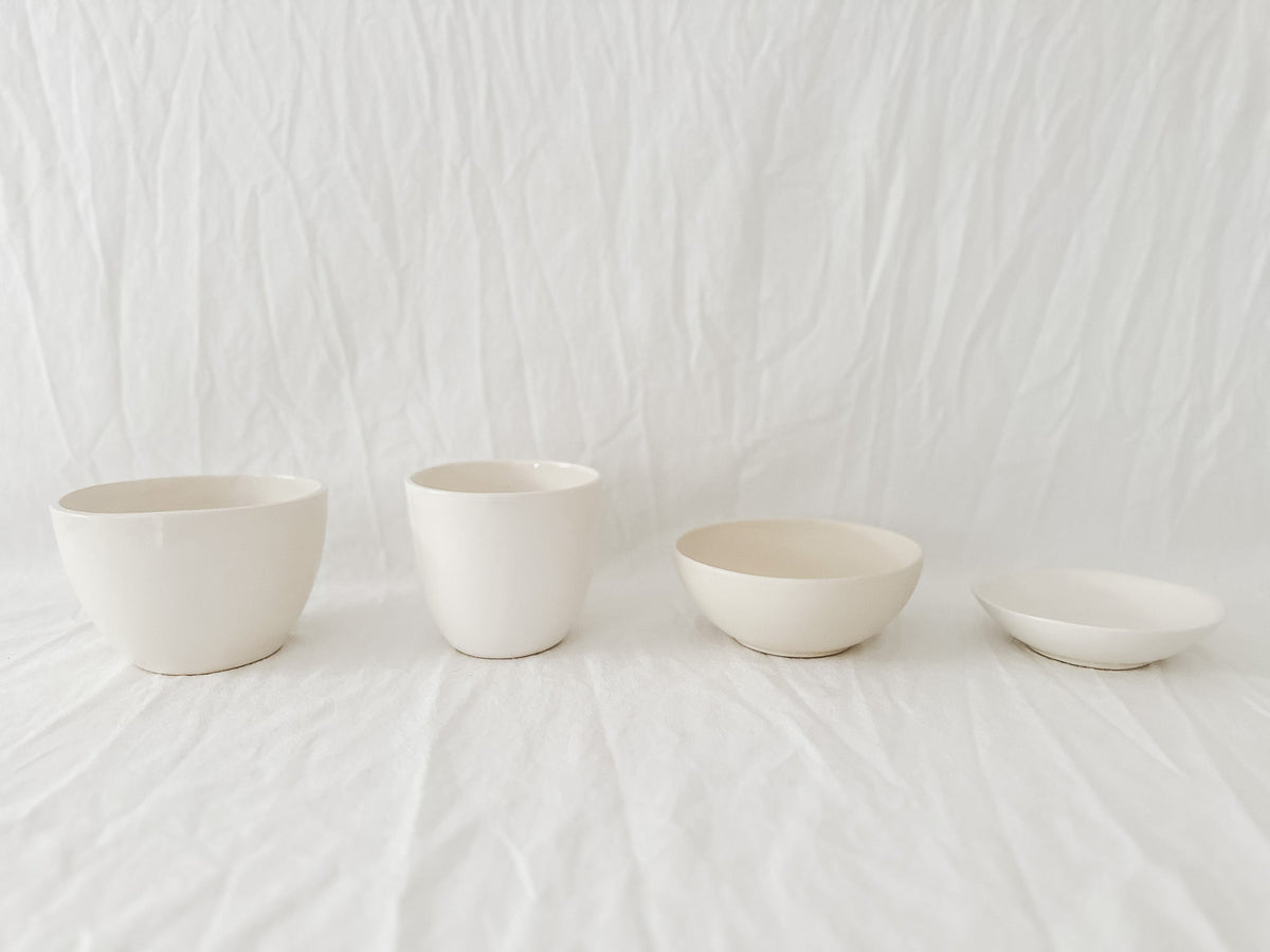 Small group of pale handmade ceramic studio samples arranged against white linen.