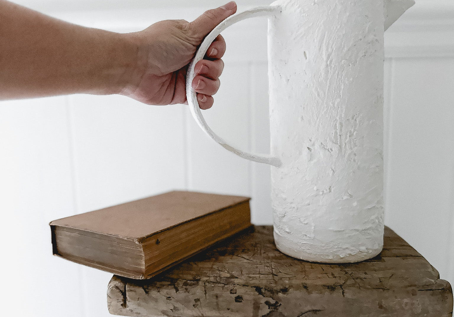 A handmade ceramic pitcher with an oversized handle, styled with fresh flowers on a sunlit kitchen counter
