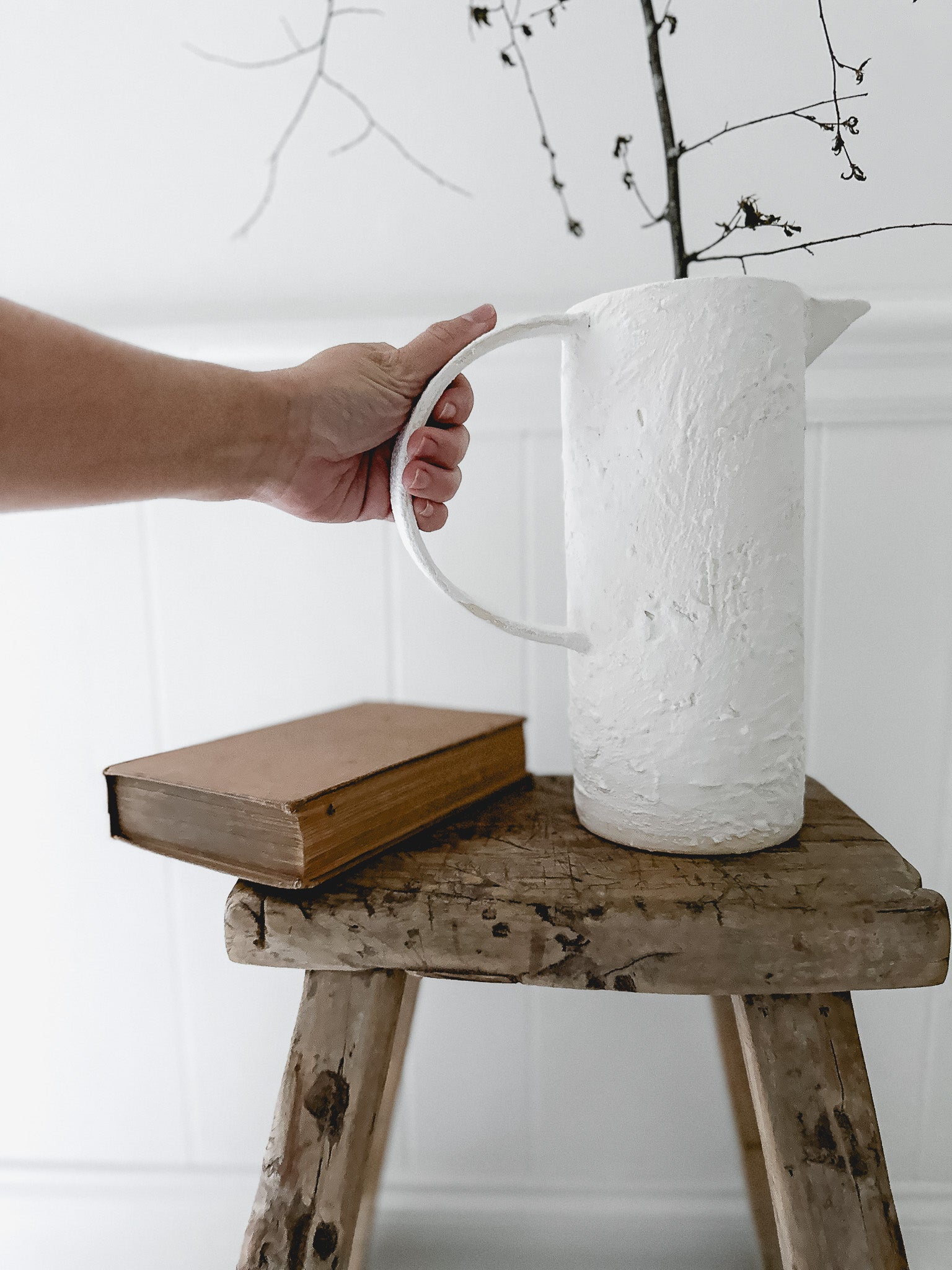 A handmade ceramic pitcher with an oversized handle, styled with fresh flowers on a sunlit kitchen counter
