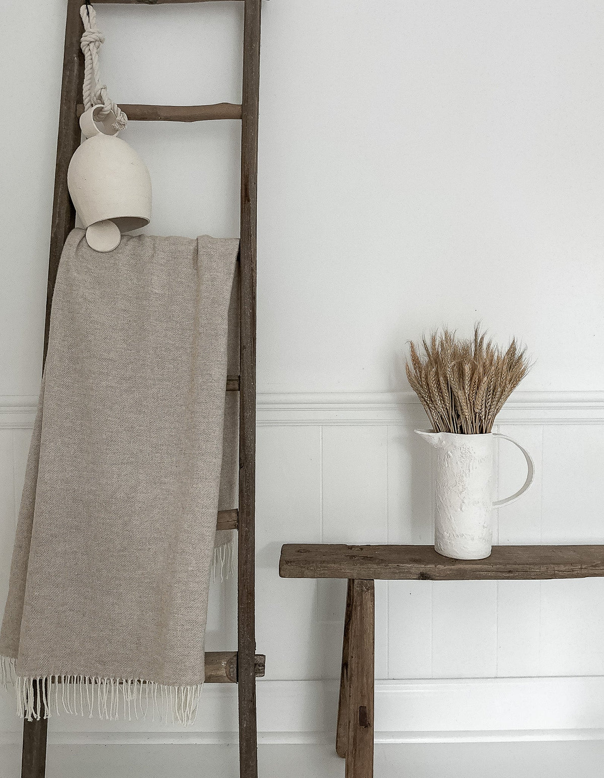 Quiet sunlit summer corner with pale pottery, natural wood, and dried stems.