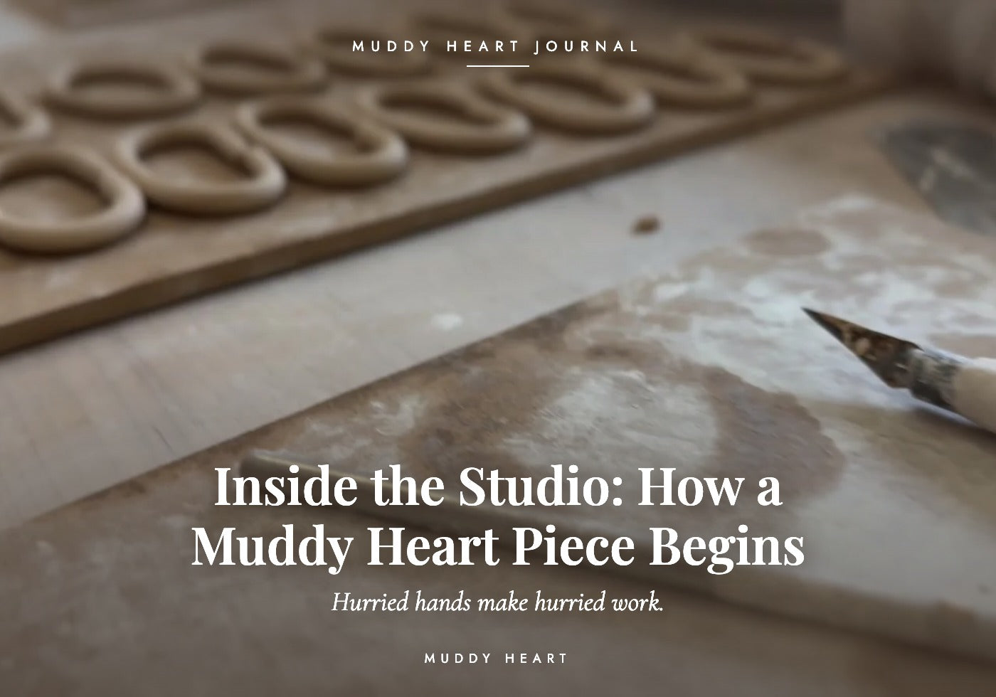 Rows of hand-pulled clay ring handles drying on a floured wooden board beside a carving tool, titled 'Inside the Studio: How a Muddy Heart Piece Begins' — Muddy Heart Journal