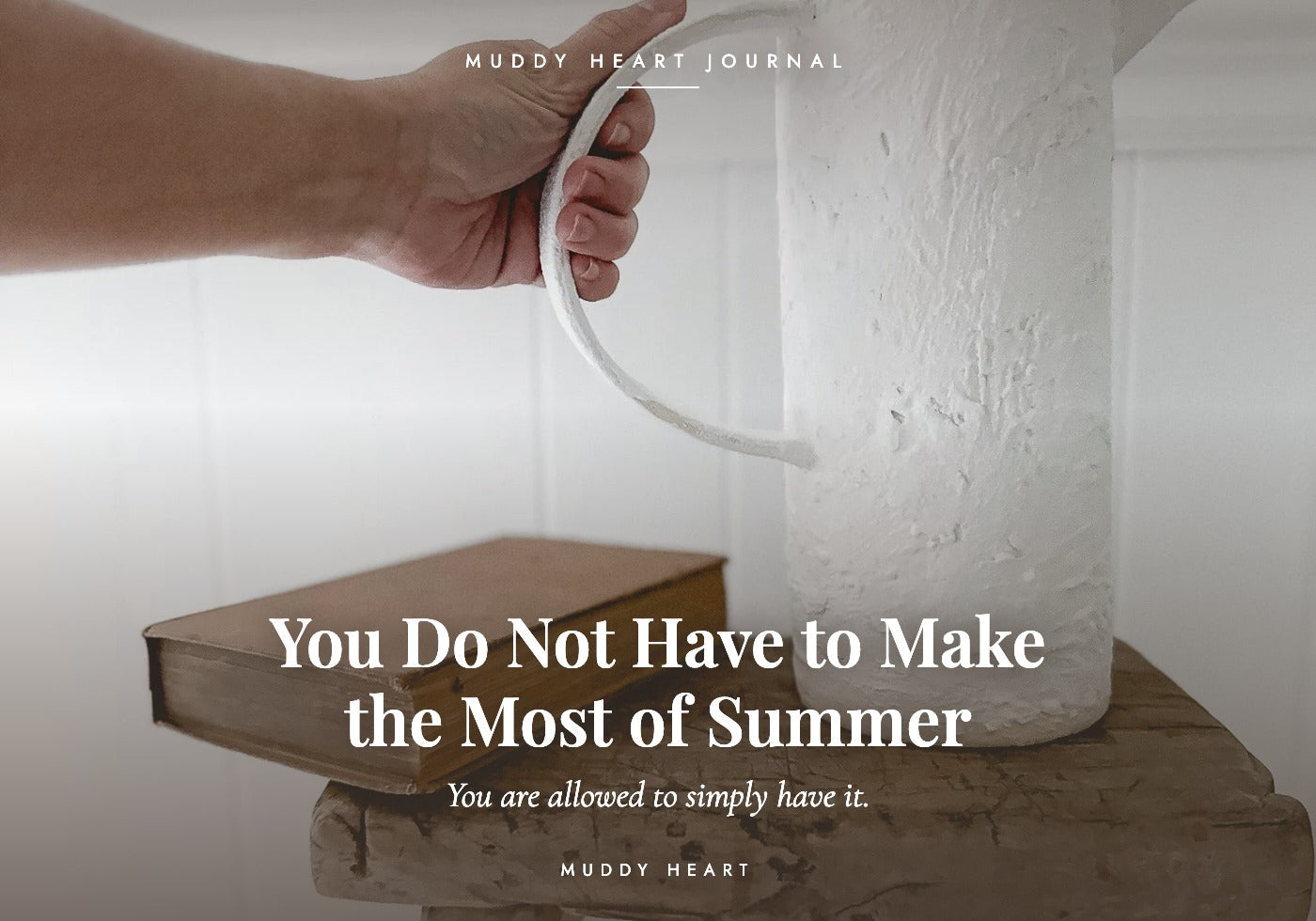 A hand gripping the oversized loop handle of a tall white textured handmade ceramic pitcher standing on an antique book, titled 'You Do Not Have to Make the Most of Summer' — Muddy Heart Journal