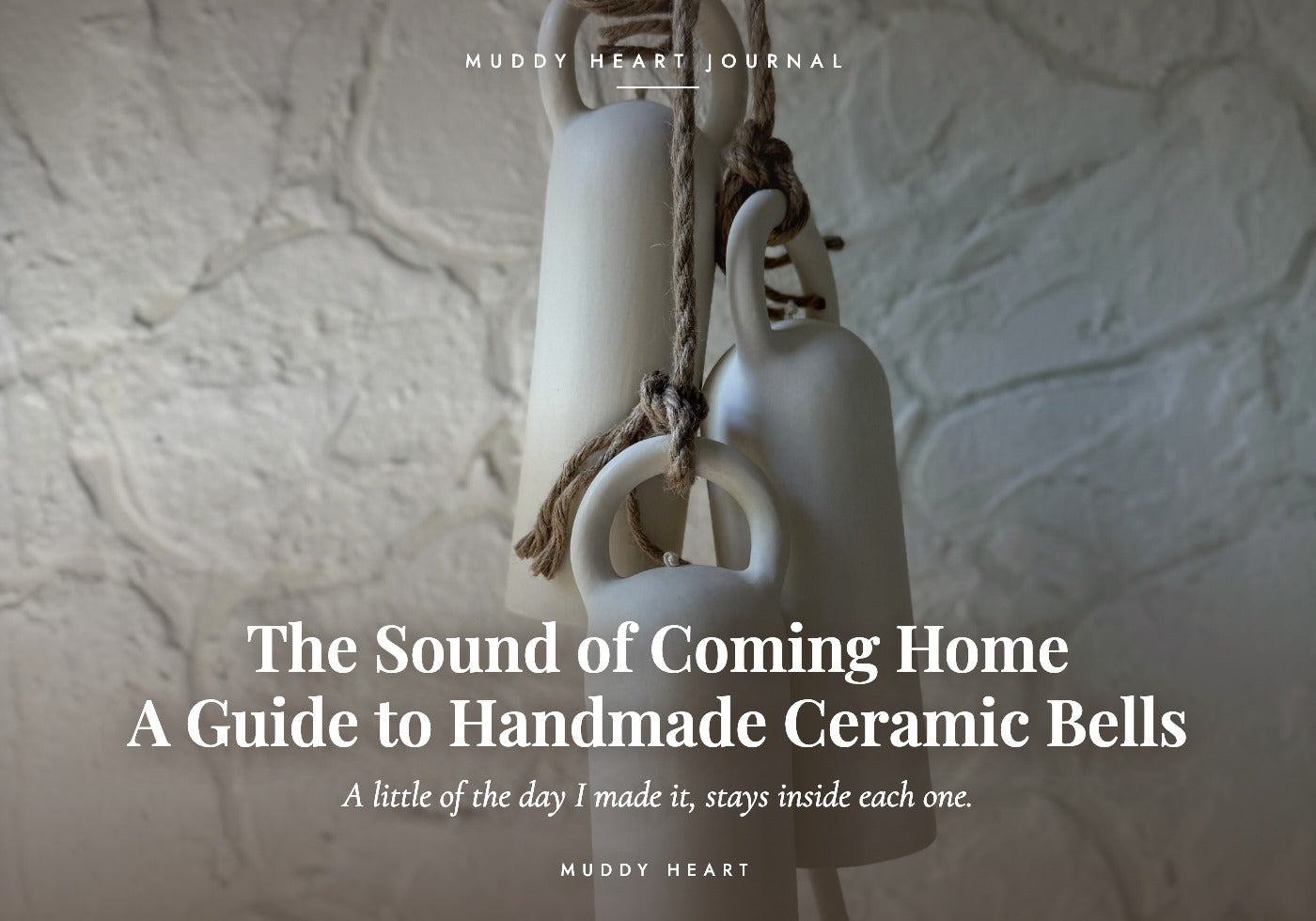 Three pale handmade ceramic bells hanging on twisted jute rope with ceramic ring knockers against a white textured plaster wall, titled 'The Sound of Coming Home: A Guide to Handmade Ceramic Bells'