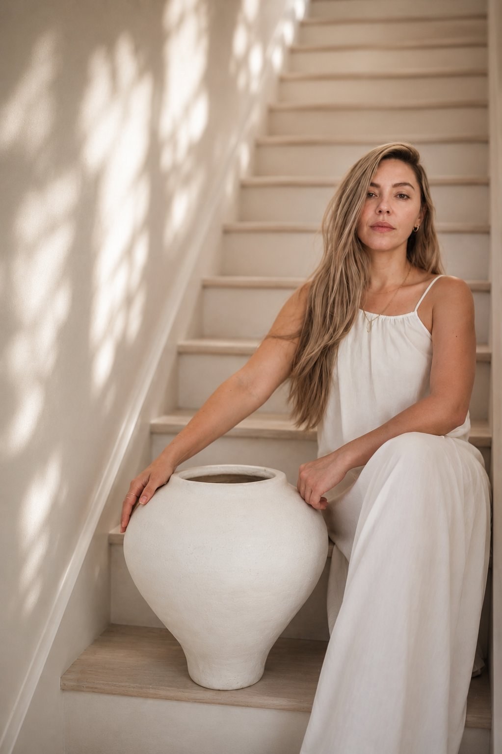 Meli, the maker behind Muddy Heart, seated on a staircase with a large handmade ceramic vessel