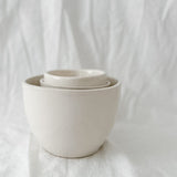 Nesting set of gloss white handmade ceramic bowls, stacked one inside another on a linen backdrop.