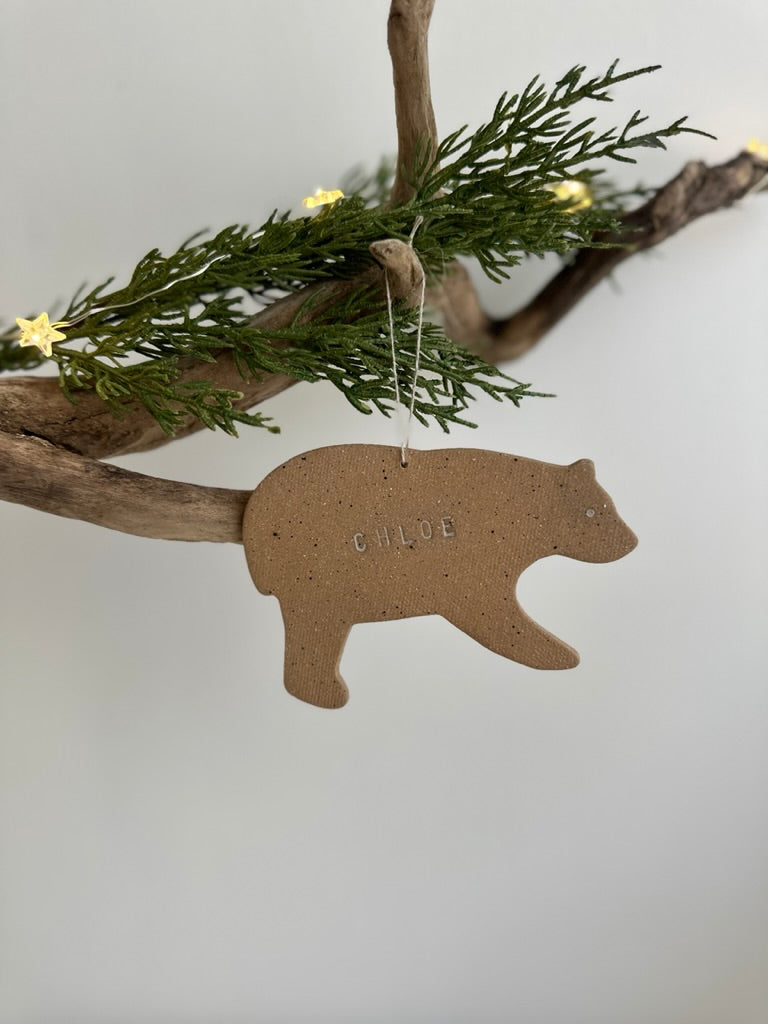 Brown bear-shaped handmade ceramic ornament hanging from a branch with greenery