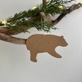 Brown bear-shaped handmade ceramic ornament hanging from a branch with greenery