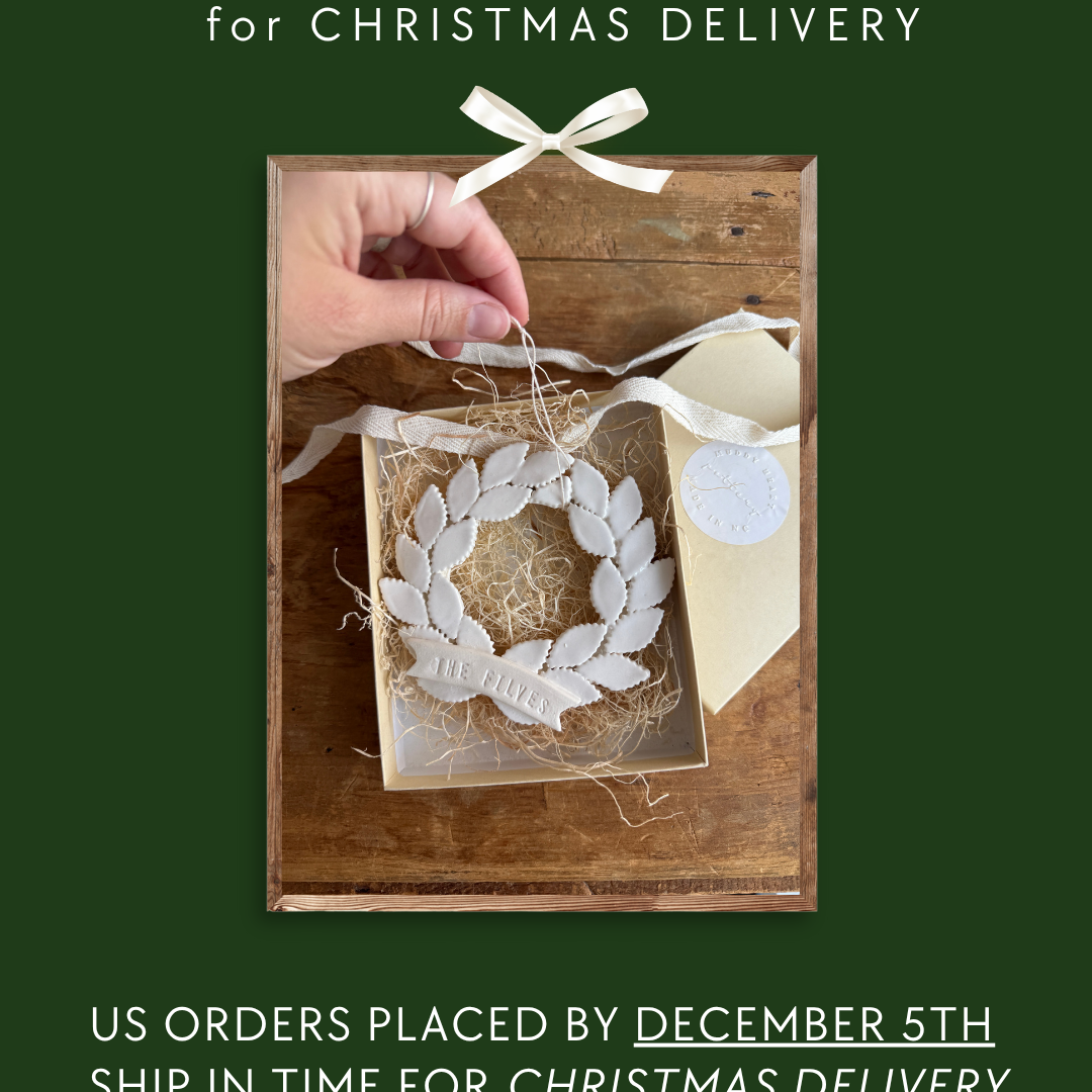The image is a promotional poster for Christmas delivery orders. It features a hand placing a white ornament into a wooden box, which is placed on a wooden surface. The text on the poster indicates that orders are placed by December 5th and that the ship will be in time for Christmas delivery. The text also mentions that orders received after December 5th will be shipped in January.