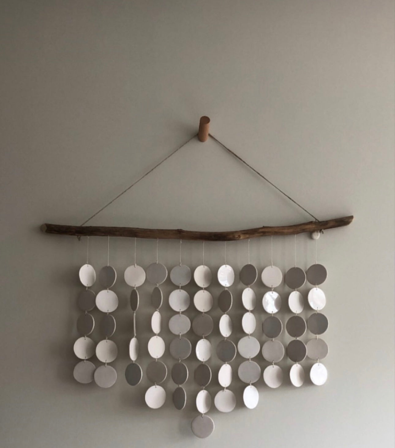 Neutral-colored ceramic disc wall hanging on driftwood