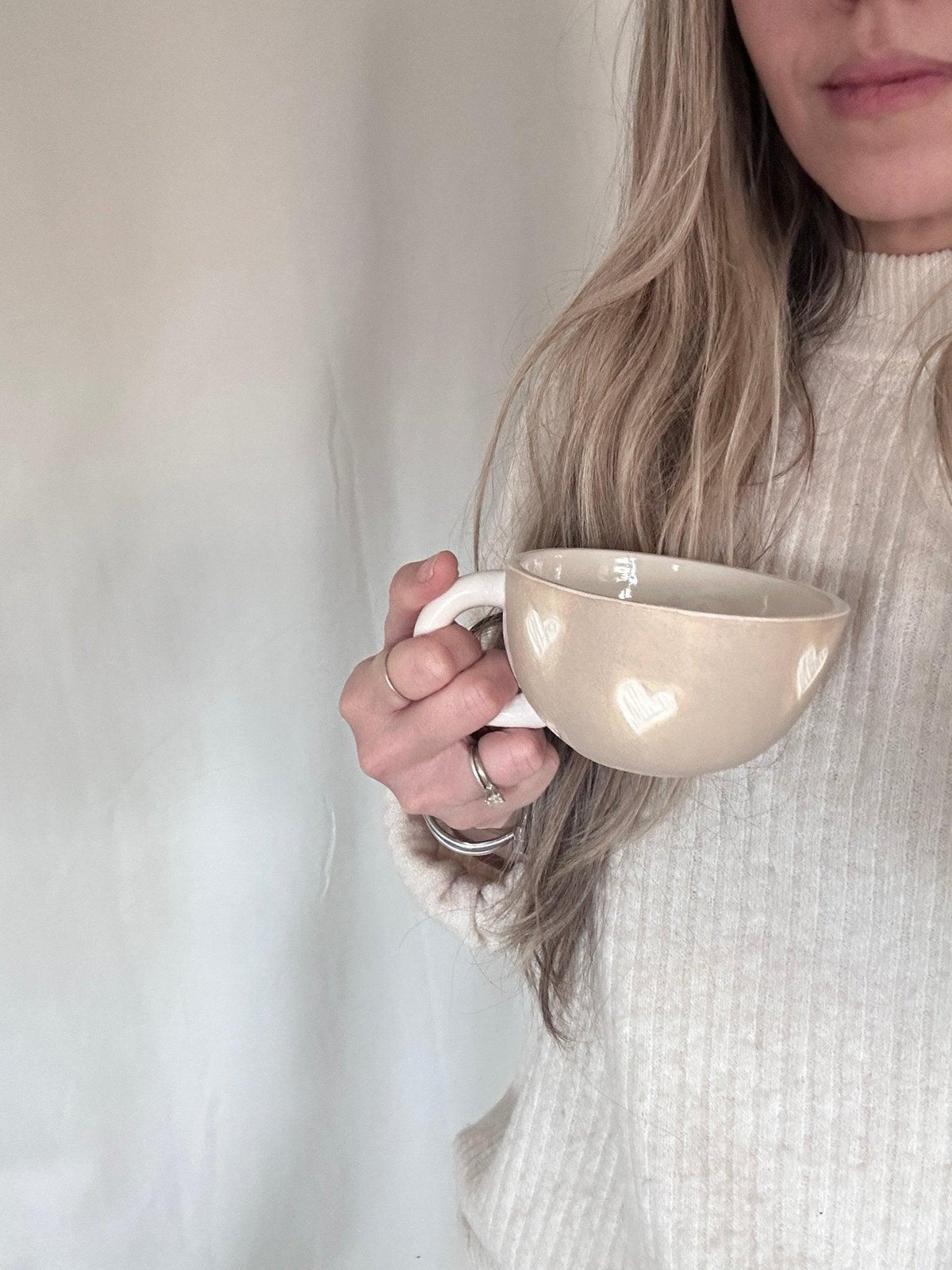 Handmade ceramic mug with hand-carved hearts in warm sand-colored clay and glossy white glaze details